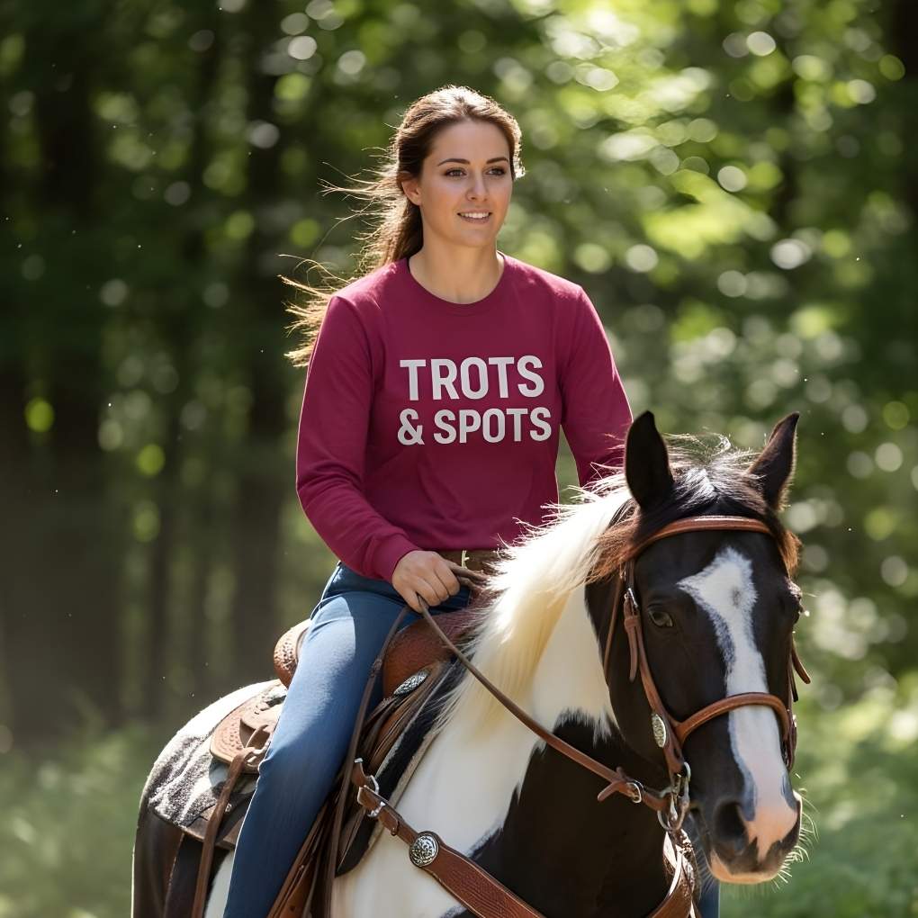 Woman riding a horse with a maroon shirt that says 'TROTS & SPOTS' in a forest setting. Trots and Spots Long Sleeve Tee for Pinto Horse Lovers, Trail Riding Tee Barn Wear