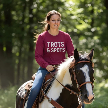 Woman riding a horse with a maroon shirt that says 'TROTS & SPOTS' in a forest setting. Trots and Spots Long Sleeve Tee for Pinto Horse Lovers, Trail Riding Tee Barn Wear