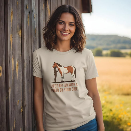 Woman wearing a t-shirt with a horse graphic and text, standing in a field. Life's Better with a Pinto T-Shirt for Pinto Horse Lovers, Trail Riding Tee for Horse Riders