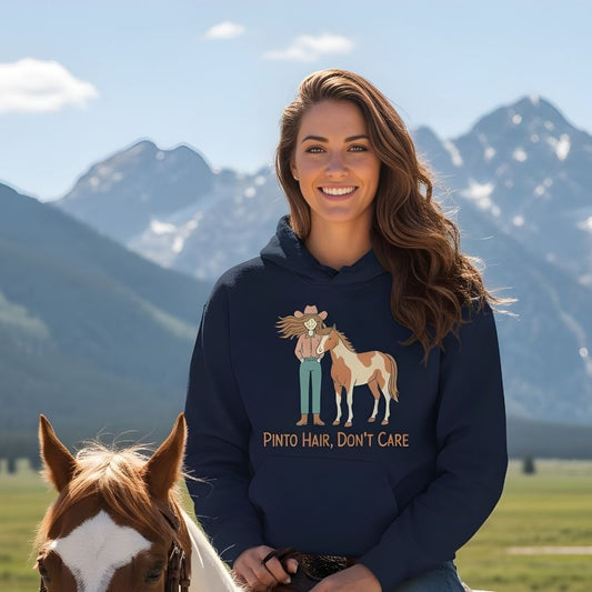 Woman wearing a hoodie with a horse graphic and text, standing in front of mountains. Pinto Hair Don't Care Hoodie for Pinto Horse Lovers, Trail Riding Hoodie