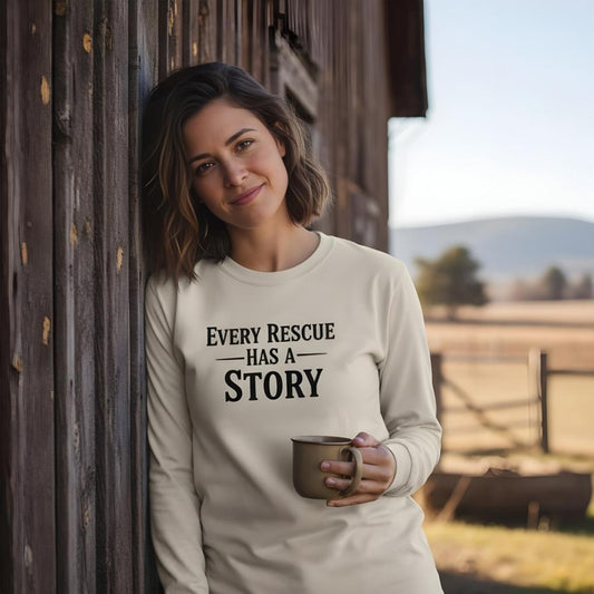 Woman wearing a sweatshirt with 'Every Rescue Has a Story' text, holding a mug, standing against a barn with a scenic background. Every Rescue has a Story Long Sleeve Tee for Horse Lovers, Horse Rescue Tee for Trail Riding