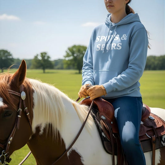 Person riding a horse wearing a hoodie with text in an outdoor setting. Spots and Spurs Hoodie for Pinto Horse Lovers, Cozy Trail Riding Hoodie