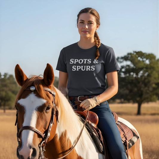 Woman riding a horse wearing a t-shirt with 'SPOTS & SPURS' text in an outdoor setting. Spots and Spurs T-Shirt for Pinto Horse Lovers, Trail Riding Tee for Horse Riders