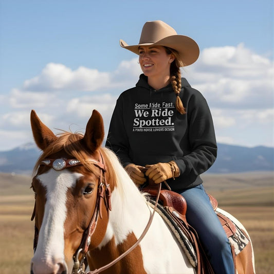 Woman riding a horse with a scenic background. We Ride Spotted Hoodie for Pinto Horse Lovers, Cozy Barn Wear Hoodie