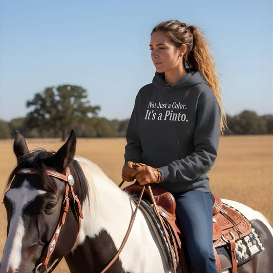 Woman riding a horse in a field wearing a hoodie with text. Not Just a Color Hoodie for Pinto Horse Lovers, Cozy Barn Wear Hoodie for Horse Riders