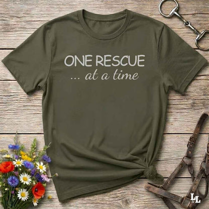 Green t-shirt with 'ONE RESCUE ... at a time' text on a wooden surface with flowers and tools.