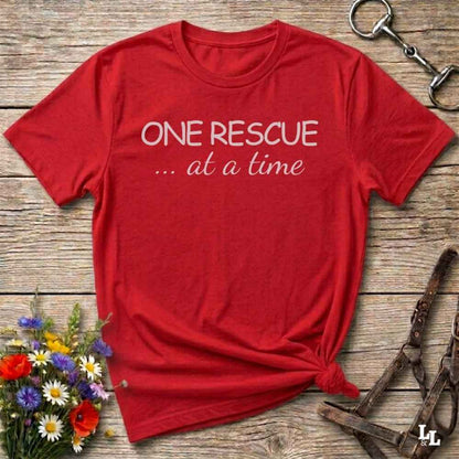 Red t-shirt with 'ONE RESCUE ... at a time' text on a wooden surface with flowers and tools.