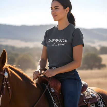 Woman riding a horse with 'One Rescue at a Time' shirt in a scenic outdoor setting. One Rescue at a Time T-Shirt Just Giving Tee, for Horse Lovers, Trail Riding Tee