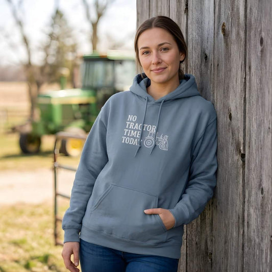 Woman wearing a blue hoodie with a tractor graphic and text, standing next to a wooden fence with a tractor in the background. No Tractor Time Today Hoodie for Horse Riders, Outdoor Hoodie Barn Wear