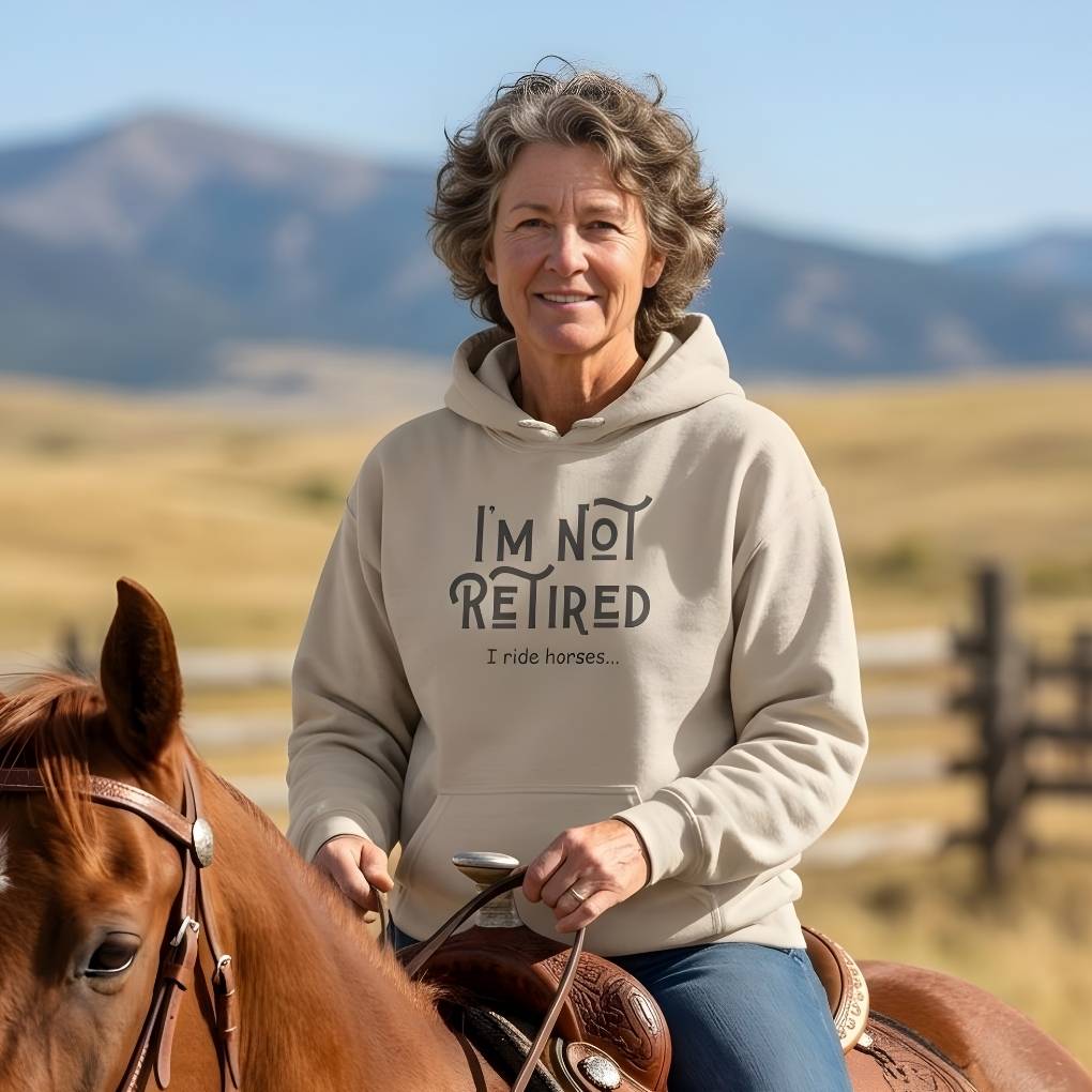 Woman in a hoodie riding a horse with mountains in the background. Pink I'm Not Retired I Ride Horses Hoodie for Horse Lovers, Cozy Hoodie for Trail Rides, perfect horse lover gift