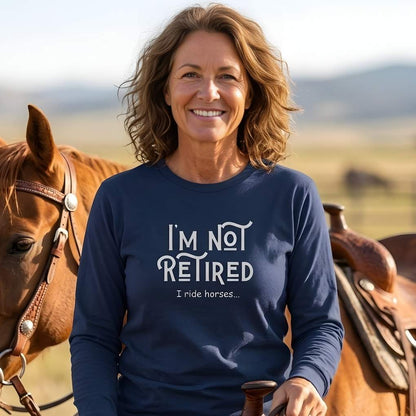 Woman wearing a navy blue sweatshirt with 'I'm not retired, I ride horses' text, standing next to a horse in a field. I'm Not Retired I Ride Horses Long Sleeve Tee for Horse Riders, Sweatshirt Trail Riding Top, perfect gift for horse lovers