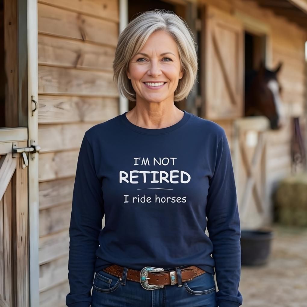 Woman wearing a navy blue sweatshirt with text standing in front of a wooden stable.   I'm Not Retired I Ride Horses Long Sleeve Tee for Horse Lovers, Trail Riding Tee, perfect gift for horse riders