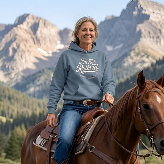 Person riding a horse with mountains in the background wearing a hoodie with text. I'm Not Retired I Ride Horses Hoodie for Horse Lovers, Horse Riding Hoodie Equestrian Wear, perfect for gifts for horse lovers