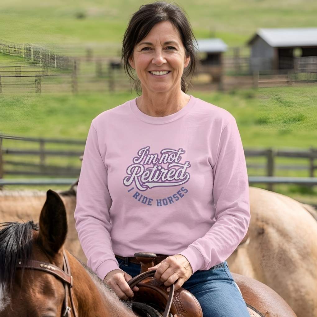 Woman riding a horse wearing a pink sweatshirt with text, set against a rural background.  I'm Not Retired I Ride Horses Long Sleeve Tee for Horse Lovers, Trail Riding Barn Wear, perfect gift for horse riders