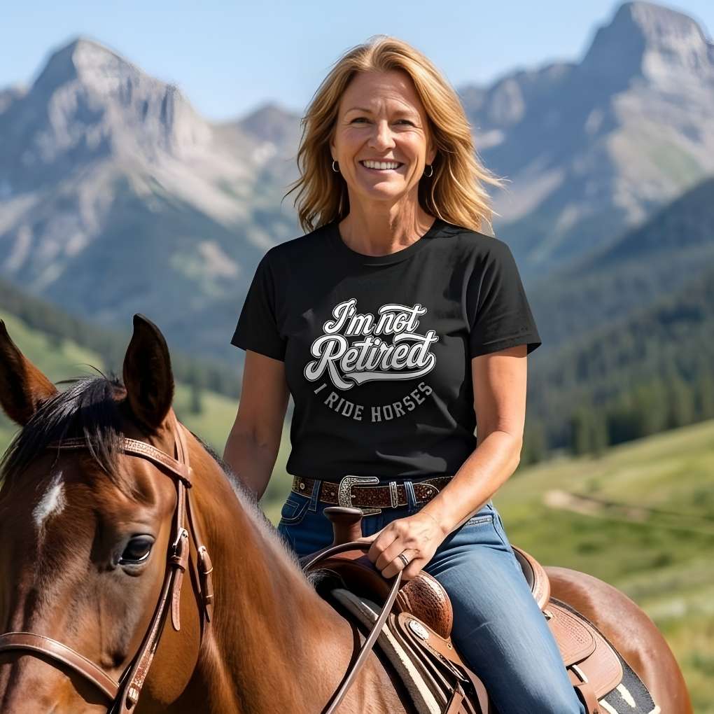 Woman riding a horse with mountains in the background wearing a black t-shirt with text. I'm Not Retired I Ride Horses T-Shirt For Horse Lovers, Trail Riding Tee, perfect gift for horse riders