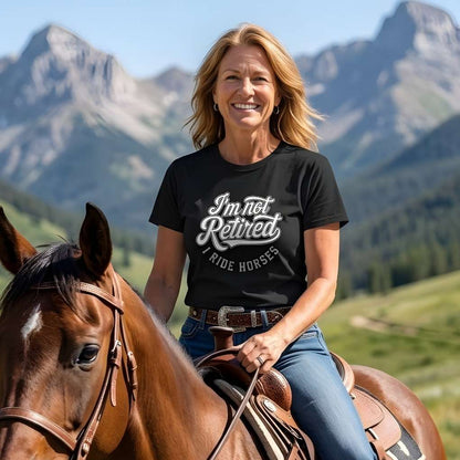 Woman riding a horse with mountains in the background wearing a black t-shirt with text. I'm Not Retired I Ride Horses T-Shirt For Horse Lovers, Trail Riding Tee, perfect gift for horse riders