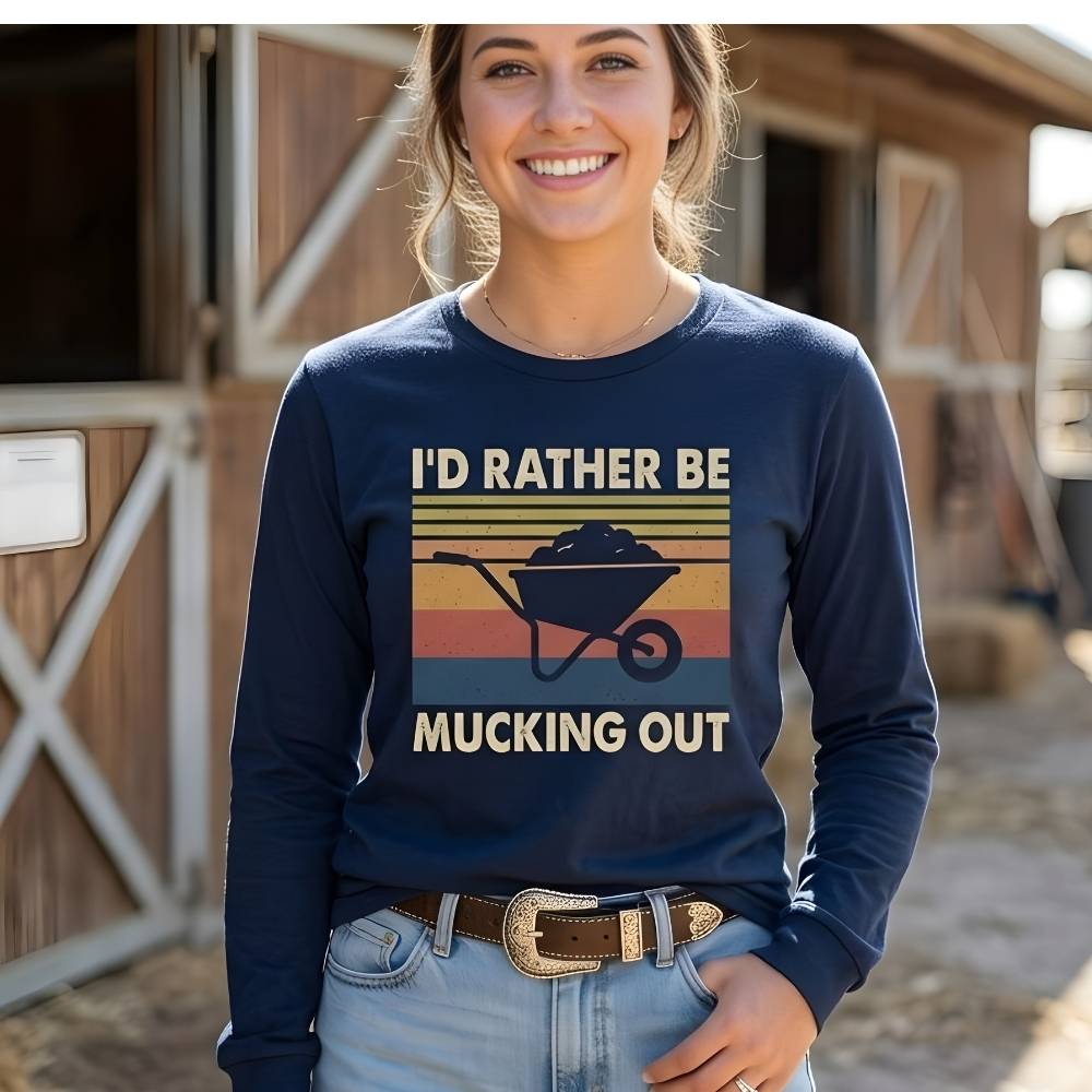 Person wearing a navy blue sweatshirt with a graphic and text, standing in front of a barn.  I'd Rather be Mucking Out Long Sleeve Tee for Horse Riders, Trail Riding Sweatshirt, perfect present for horse riders