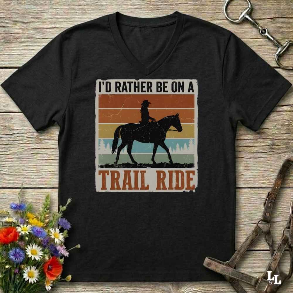 A black V-neck t-shirt with a retro western graphic of a cowboy riding a horse, styled on a wooden background with equestrian accessories and flowers.