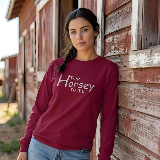 Woman wearing a maroon sweatshirt with 'Talk Horsey to me...' text, leaning against a wooden barn. Talk Horsey to Me Long Sleeve Tee for Horse Lovers, Trail Riding Tee, perfect gift for horse riders, mothers day gift, fathers day gift, Xmas gift