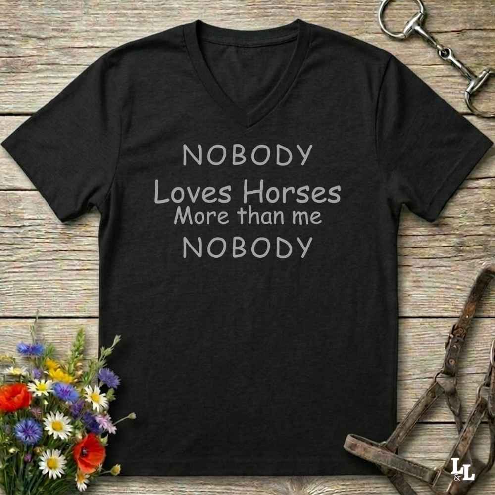A black V-neck t-shirt with the text 'NOBODY Loves Horses More than me NOBODY' printed in white on the front, displayed on a rustic wooden background with equestrian-themed props.