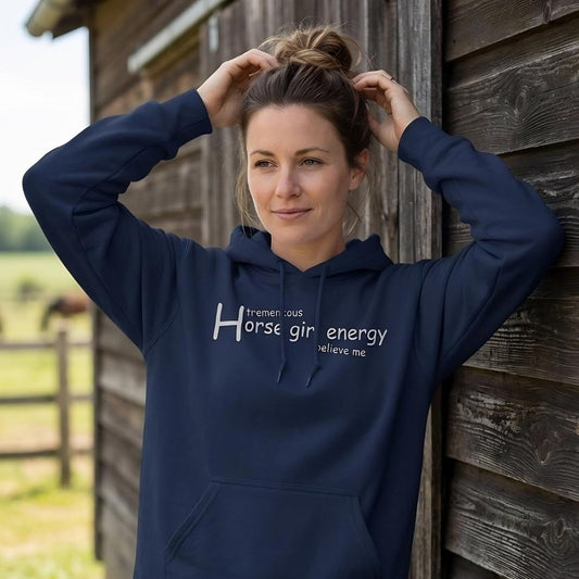 Woman wearing a navy hoodie with text, standing against a wooden barn with a horse in the background. Horse Girl Energy Hoodie for Horse Lovers, Cozy Trail Riding Hoodie, Equestrian Top. Perfect gift for horse riders, birthday present for horse lovers, Xmas present for horse lovers, mothers day gift