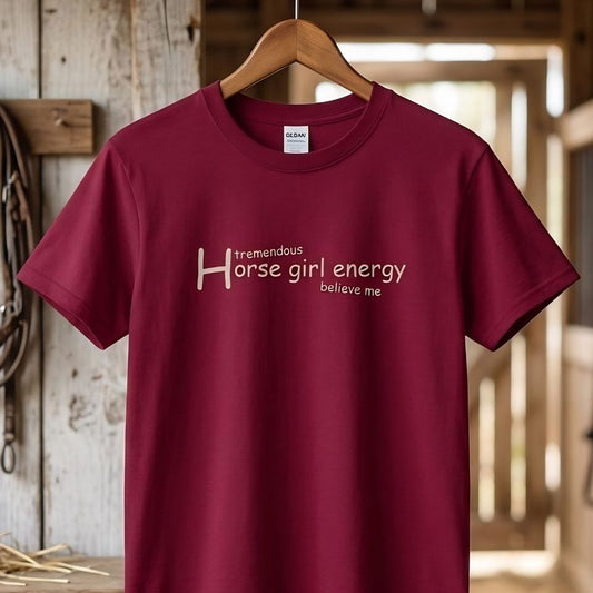 Maroon t-shirt with 'Horse girl energy believe me' text on a wooden hangerin a barn. Horse Girl Energy T-Shirt gift for Horse Riders, Horse Lover Tee, Trail Riding Top. Perfect gift for horse lover, gift for mothers day, xmas gift for horse riders.
