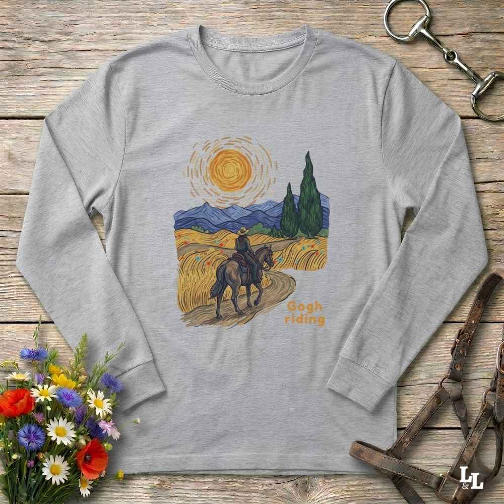 A light heather gray long-sleeve t-shirt with a colorful 'Rough Riding' graphic inspired by Van Gogh's Starry Night, laid flat on a rustic wooden background with decorative equestrian and floral props.