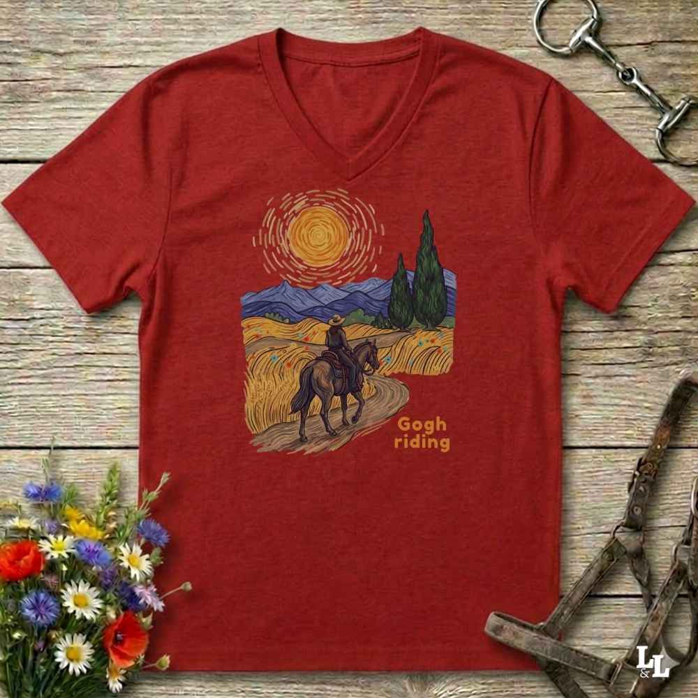 Red v-neck tee with van gogh inspired design and the words Gogh Riding, lying on barn style floorboards with flowers and horse halter and horse bit