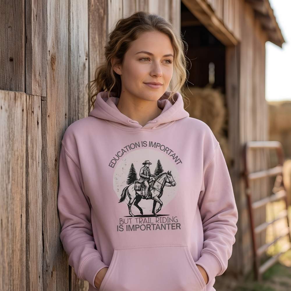 Woman wearing a pink hoodie with a horse and rider graphic and text, standing in front of a wooden barn. Education is Important Hoodie for Horse Lovers, Perfect gift for Horse Rider, horse girl hoodie, horse mom hoodie, horse lover, horse girl, Funny horse lover gifts, Funny horse hoodies, Horse girl gifts, Equestrian graphic hoodies, fathers day gift, Sarcastic horse hoodie.