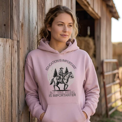 Woman wearing a pink hoodie with a horse and rider graphic and text, standing in front of a wooden barn. Education is Important Hoodie for Horse Lovers, Perfect gift for Horse Rider, horse girl hoodie, horse mom hoodie, horse lover, horse girl, Funny horse lover gifts, Funny horse hoodies, Horse girl gifts, Equestrian graphic hoodies, fathers day gift, Sarcastic horse hoodie.