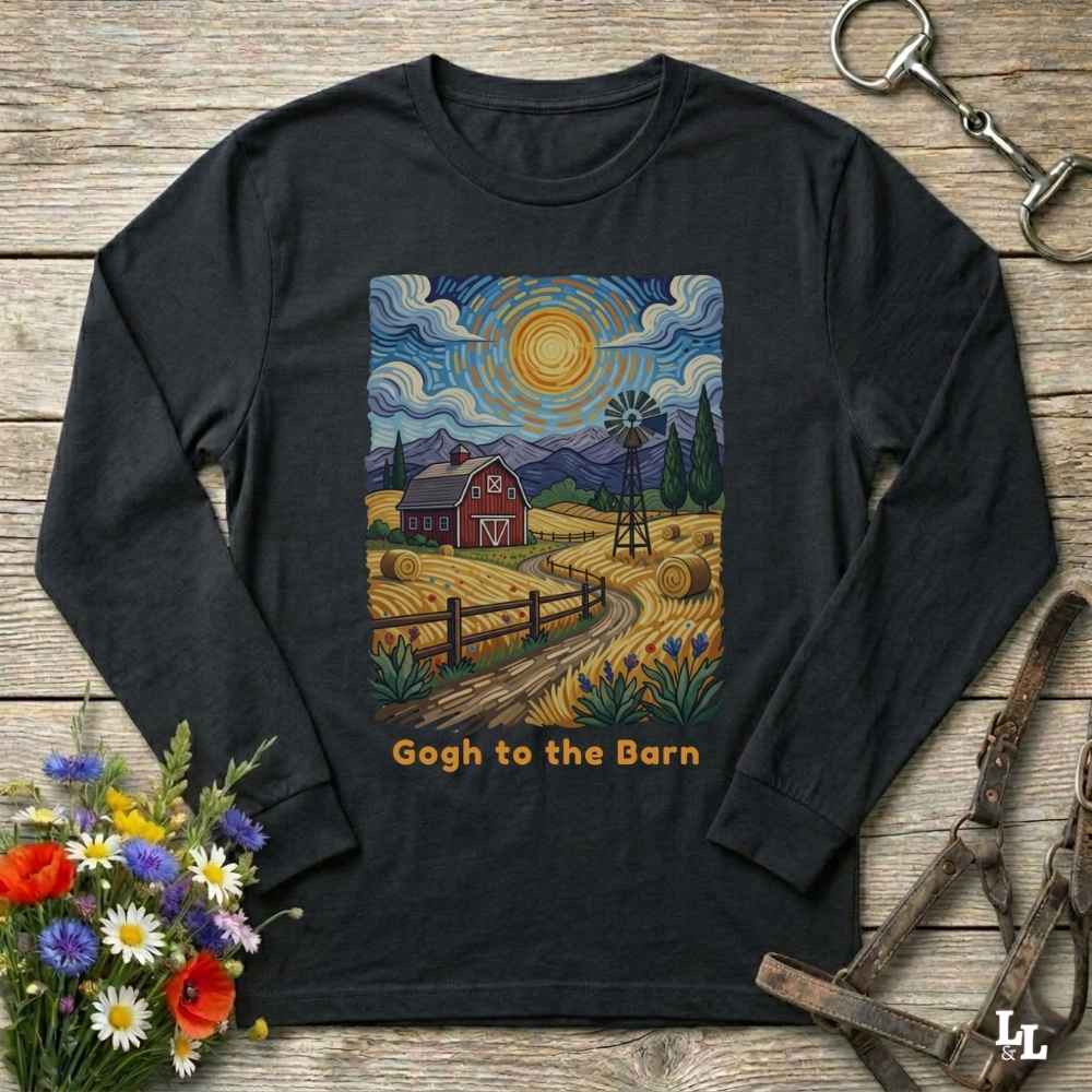 A black long-sleeve t-shirt with a colorful barn farm landscape graphic in a Van Gogh style, featuring the text 'Gogh to the Barn' below it. The shirt is displayed flat on a rustic wooden background with decorative flowers and horse tack.