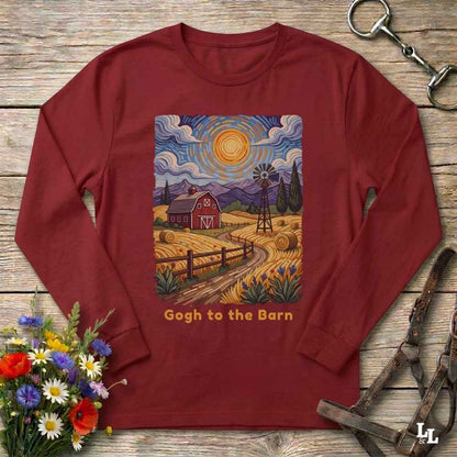 A long-sleeve crewneck t-shirt in maroon red, laid flat on a rustic wooden surface. The shirt features a colorful graphic print in the center depicting a stylized, swirling Van Gogh-inspired farm landscape with a barn, windmill, haystacks, and mountains under a bright sun.