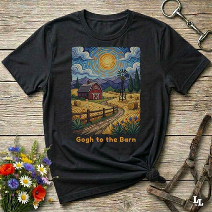 A black graphic t-shirt laid flat on a rustic wooden surface, styled with flowers, a horse bit, and a leather halter. The t-shirt features a colorful art print in a Van Gogh-inspired style showing a red barn, a windmill, and a yellow sun, with the text 'Gogh to the Barn' printed below.