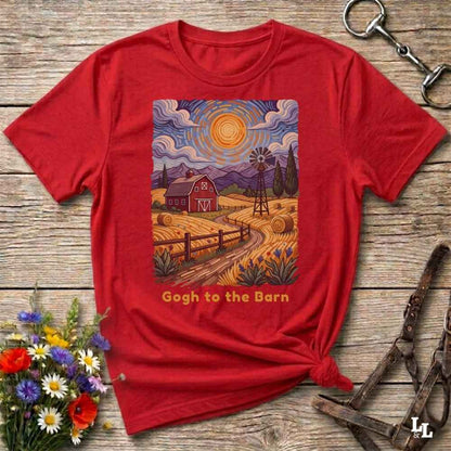 A red short-sleeve graphic T-shirt laid flat on a rustic wooden surface, styled with flowers, a horse bit, and a leather bridle. The shirt features a colorful barn scene print with the text 'Gogh to the Barn' below it.