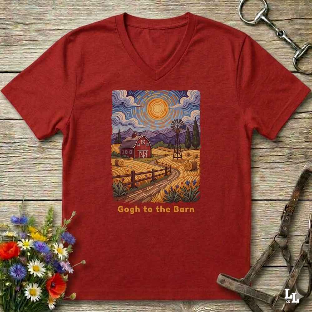 A red V-neck t-shirt laid flat on a rustic wooden surface, featuring a colorful Gogh-inspired barn landscape graphic on the chest with the text 'Gogh to the Barn'. The shirt is styled with equestrian tack and a small flower bouquet.