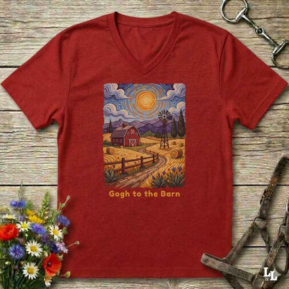 A red V-neck t-shirt laid flat on a rustic wooden surface, featuring a colorful Gogh-inspired barn landscape graphic on the chest with the text 'Gogh to the Barn'. The shirt is styled with equestrian tack and a small flower bouquet.