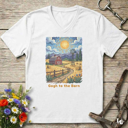 A white V-neck t-shirt laid flat on a rustic wooden surface, featuring a colorful Van Gogh-inspired barn scene graphic with the text 'Gogh to the Barn'. The shirt is styled with equestrian props (reins and a bit) and a small bouquet of wildflowers.