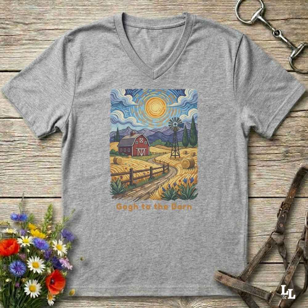 grey V-neck t-shirt laid flat on a rustic wooden surface, featuring a colorful Van Gogh-inspired barn scene graphic with the text 'Gogh to the Barn'. The shirt is styled with equestrian props (reins and a bit) and a small bouquet of wildflowers.