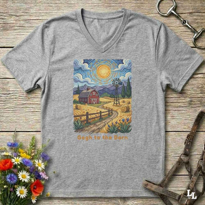 grey V-neck t-shirt laid flat on a rustic wooden surface, featuring a colorful Van Gogh-inspired barn scene graphic with the text 'Gogh to the Barn'. The shirt is styled with equestrian props (reins and a bit) and a small bouquet of wildflowers.