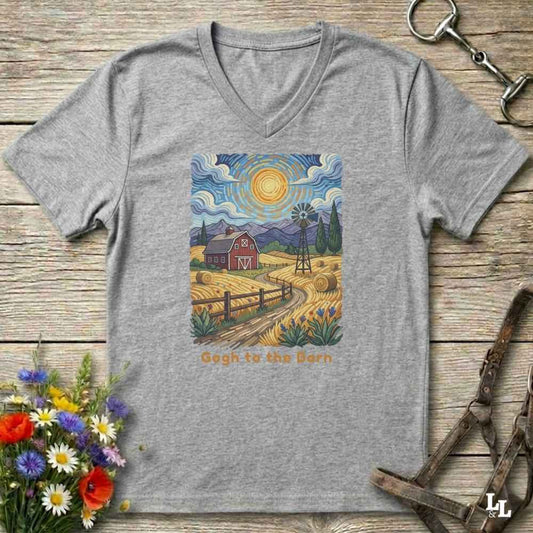 grey V-neck t-shirt laid flat on a rustic wooden surface, featuring a colorful Van Gogh-inspired barn scene graphic with the text 'Gogh to the Barn'. The shirt is styled with equestrian props (reins and a bit) and a small bouquet of wildflowers.