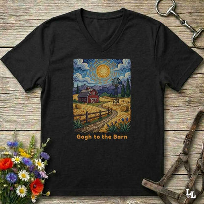 black V-neck t-shirt laid flat on a rustic wooden surface, featuring a colorful Van Gogh-inspired barn scene graphic with the text 'Gogh to the Barn'. The shirt is styled with equestrian props (reins and a bit) and a small bouquet of wildflowers.