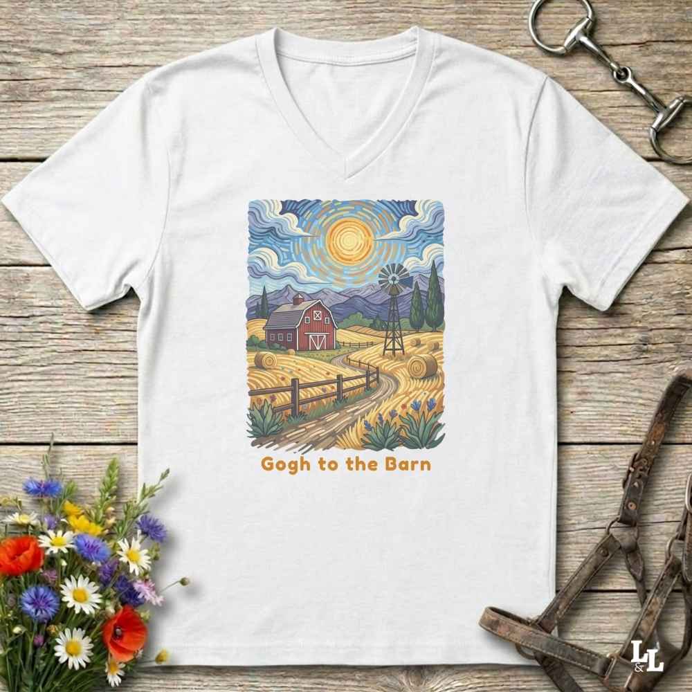 white V-neck t-shirt laid flat on a rustic wooden surface, featuring a colorful Van Gogh-inspired barn scene graphic with the text 'Gogh to the Barn'. The shirt is styled with equestrian props (reins and a bit) and a small bouquet of wildflowers.