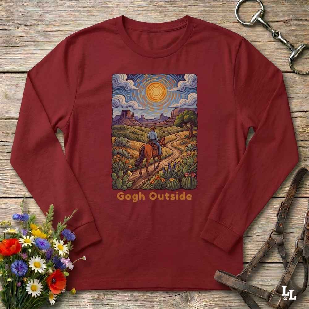 A long-sleeve crewneck t-shirt in maroon red, laid flat on a rustic wooden surface. The shirt features a colorful graphic print in the center depicting a desert landscape with a rider on a horse, cacti, and a sun, with the text 'Gogh Outside' printed below.