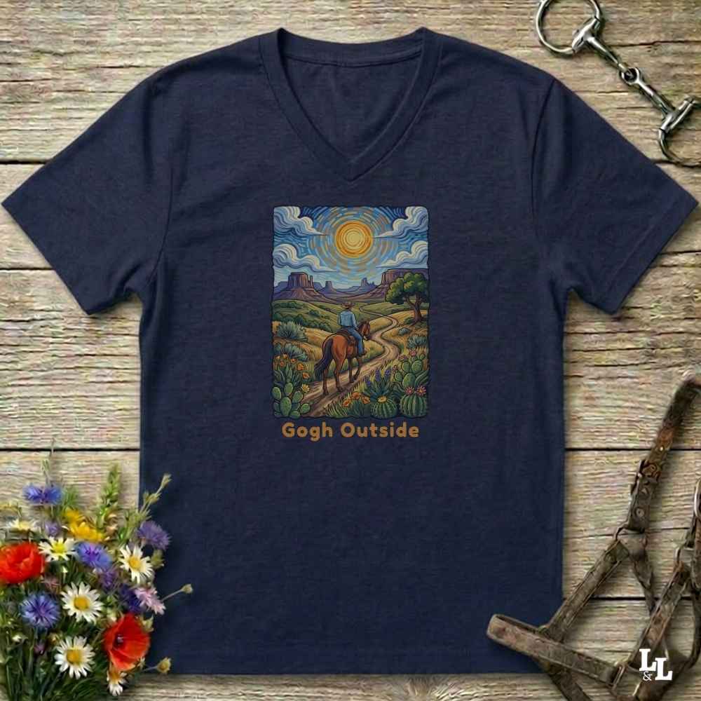 navy blue V-neck t-shirt laid flat on a rustic wooden surface, featuring a colorful art print of a rider on a horse under a bright sun with the text 'Gogh Outside'. The shirt is styled with equestrian tack and wildflowers.
