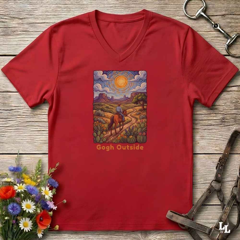 red V-neck t-shirt laid flat on a rustic wooden surface, featuring a colorful art print of a rider on a horse under a bright sun with the text 'Gogh Outside'. The shirt is styled with equestrian tack and wildflowers.