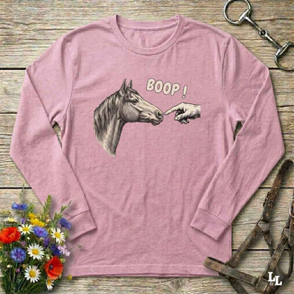Pink long-sleeve shirt with horse and hand graphic and 'BOOP!' text on a wooden surface with floral and equestrian elements.