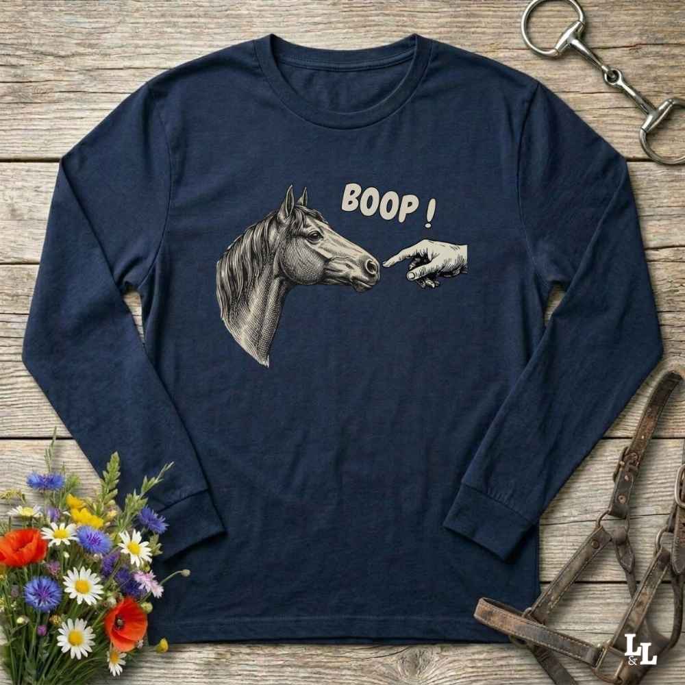 Navy blue long-sleeve shirt with horse graphic and 'BOOP!' text on a wooden surface with floral and equestrian accessories.