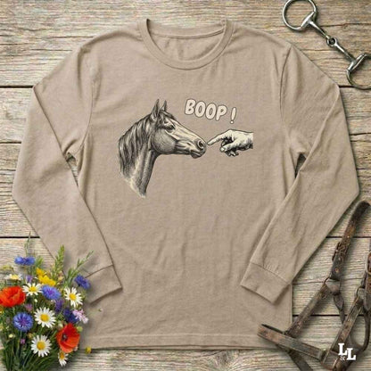 Beige long-sleeve shirt with horse graphic and 'BOOP!' text on a wooden surface with floral and equestrian accessories.