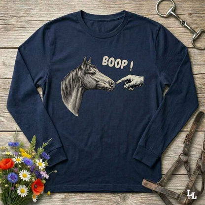 A navy blue long-sleeve t-shirt with a graphic of a horse head and a pointing hand with the text 'BOOP!' printed on the front, displayed on a rustic wooden background with equestrian accessories and flowers.