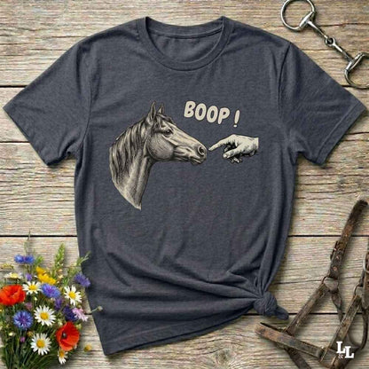 A dark heather gray graphic t-shirt laid flat on a rustic wooden surface. The shirt features a graphic of a horse head reaching towards a pointing hand with the text 'BOOP!' in beige.